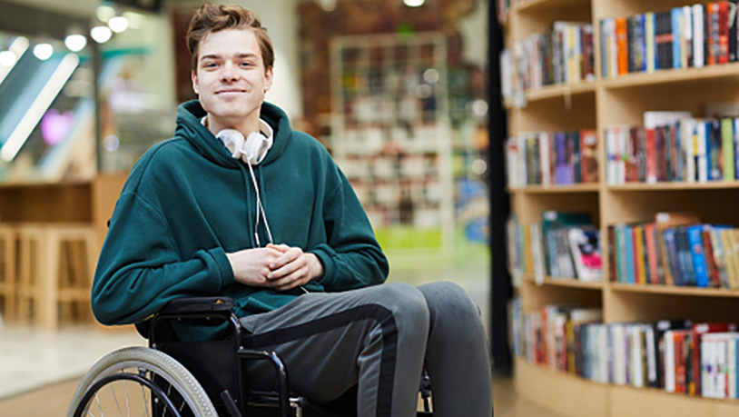 A smiling male student sits in a wheel chair in the library
