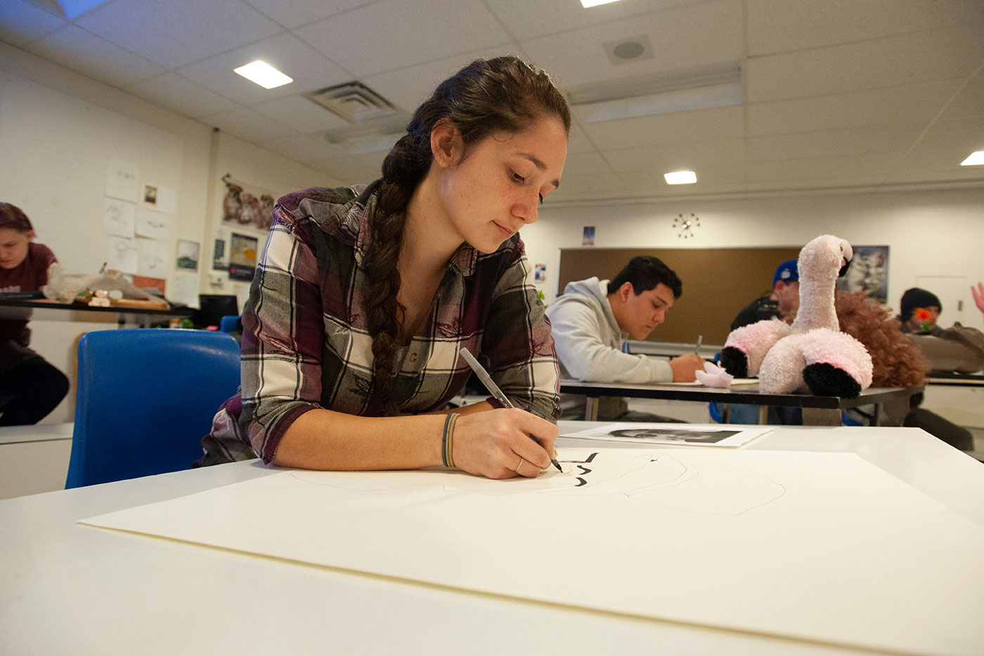 a student sits at a desk drawing on a piece of paper