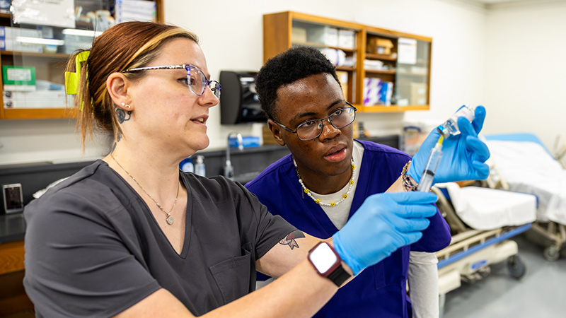 An MCC pharmacy tech instructor demonstrates how to prepare a syringe with medication for injection.