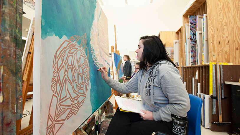 student standing in front of large canvas painting