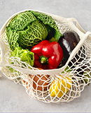 a cabbage, an eggplant and a pepper in a string bag