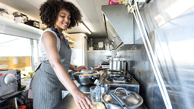 A smiling woman wearing an apron in a food truck kitchen preparing food