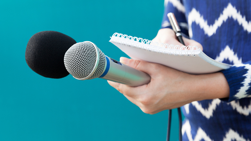 a reporter holding a microphone writing in a notebook