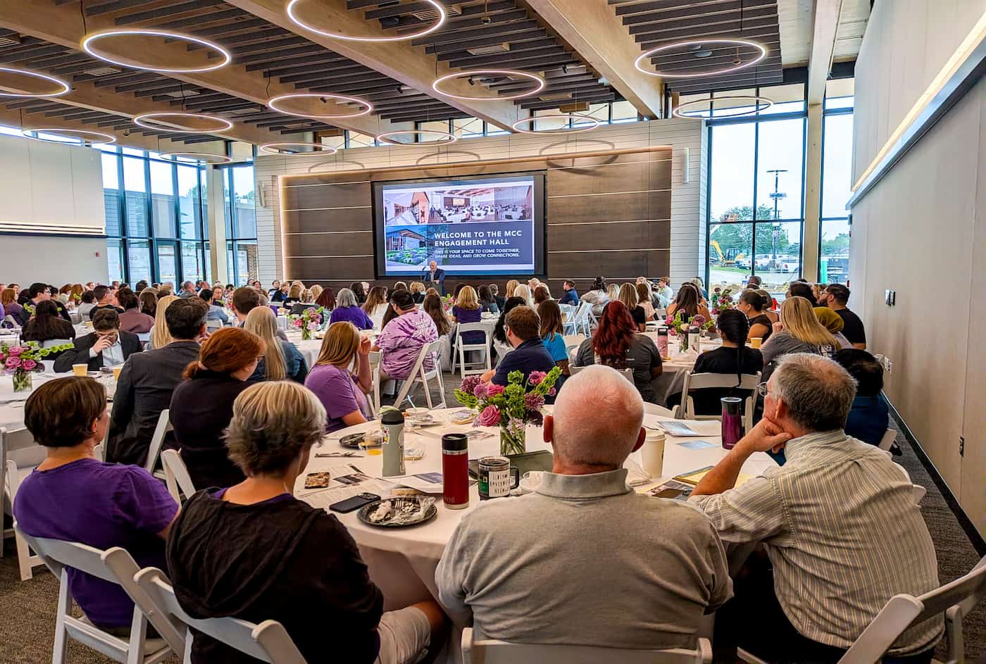 Attendees at the opening of MCC's new Engagement Hall are focused on a welcome slide.