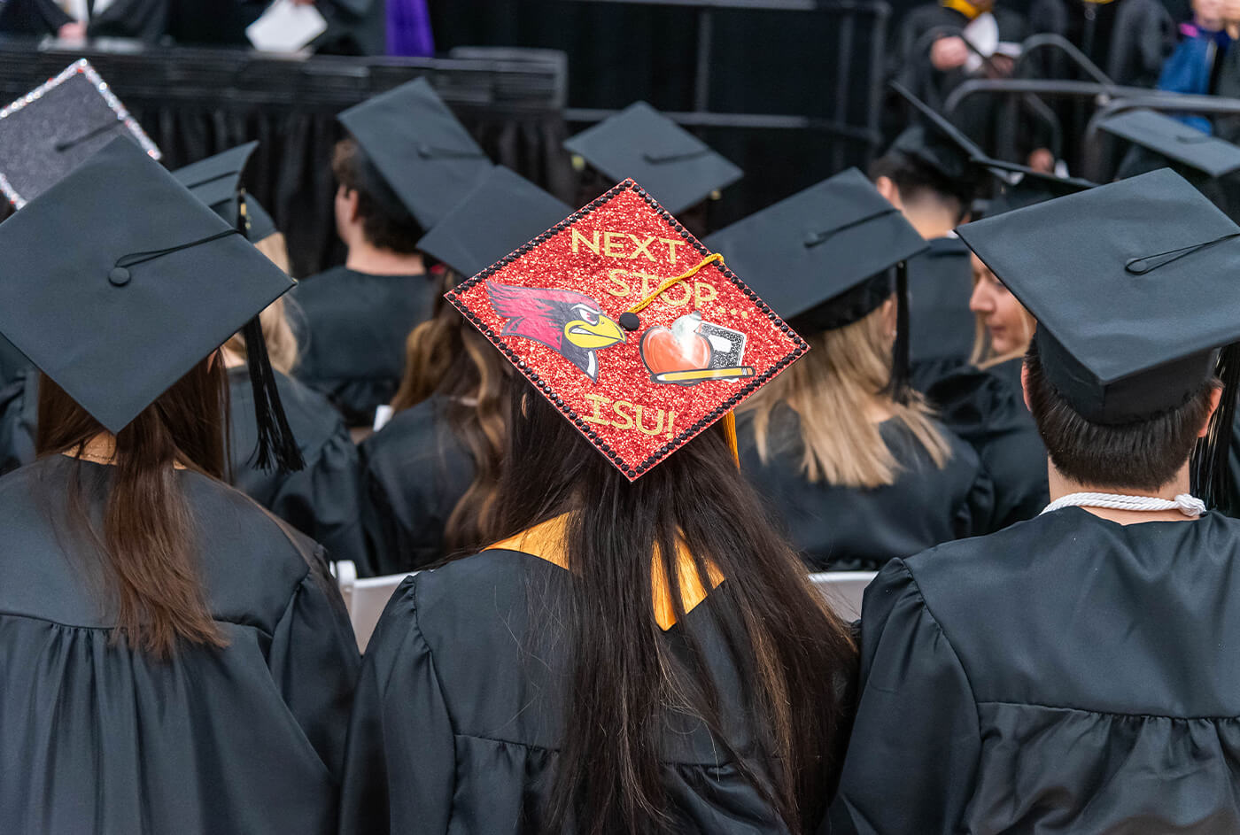 an overhead picture of graduation caps with one student's red cap decorated for ISU in the middle