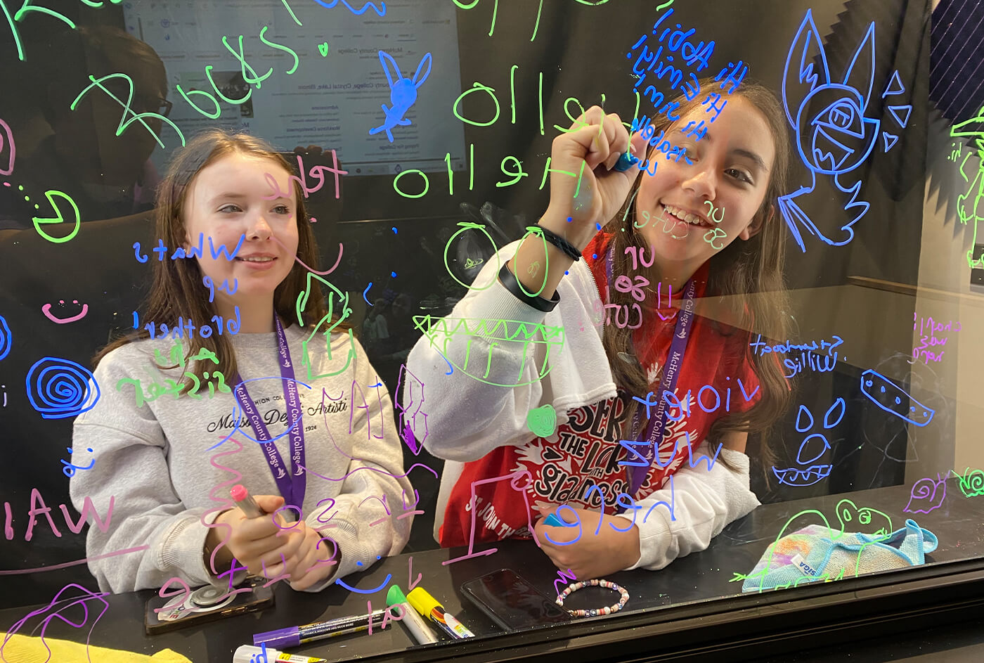 two children color using colorful markers to write on a glass panel