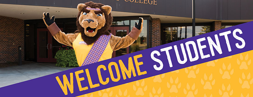 The MCC mascot, Roary the lion, stands before the door to building B. A banner says Welcome Students.