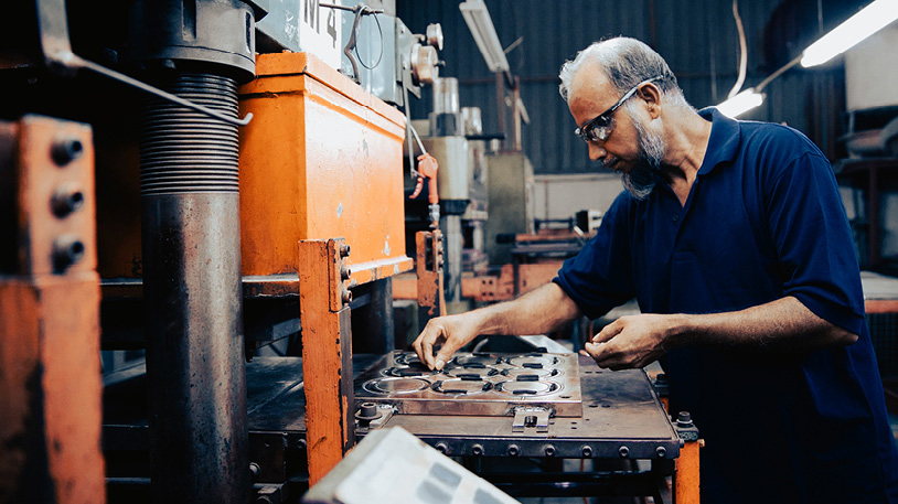 A middle-aged man wearing safety glasses operates a large industrial machine in a factory setting.