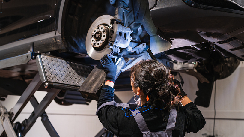 Female mechanic works on a car that is up on a lift. She faces away from the camera