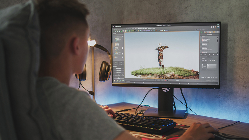 A person working on a 3D modeling project of a character standing on grass using a computer with design software open.