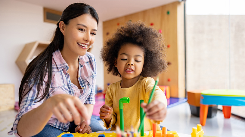 Young woman and child playing with colorful building blocks together indoors, sharing a joyful moment of creativity.