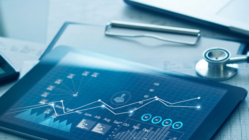 Tablet displaying a digital financial graph with monthly data points and analytics overlays on a desk with a stethoscope nearby.