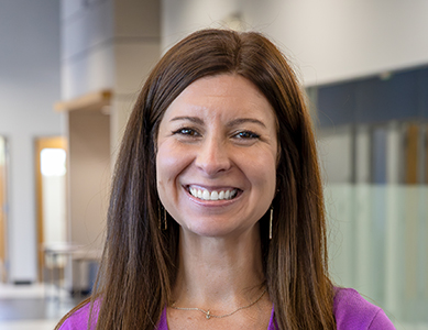 Kailley Harmon, Executive Director of the University Center at MCC, smiles in a modern office, wearing a purple cardigan and a white top.