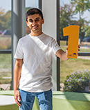 MCC student Humza Bangash stands in the lobby of the Liebman Science Center holding a number 1. 
