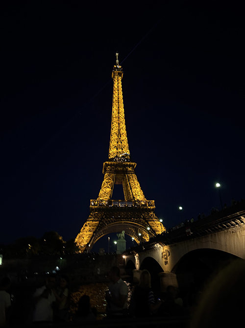 Eiffel Tower illuminated at night, seen from a river viewpoint.