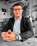 MCC student Jason Ramirez wearing a dress shirt and suit coat sitting at a desk