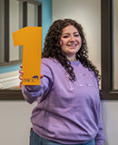 MCC student Taiya Stewart stands in front of a clinical lab holding a number 1. 