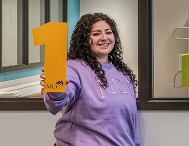 MCC nursing student Taiya Stewart stands in front of a clinical lab holding a number 1. 